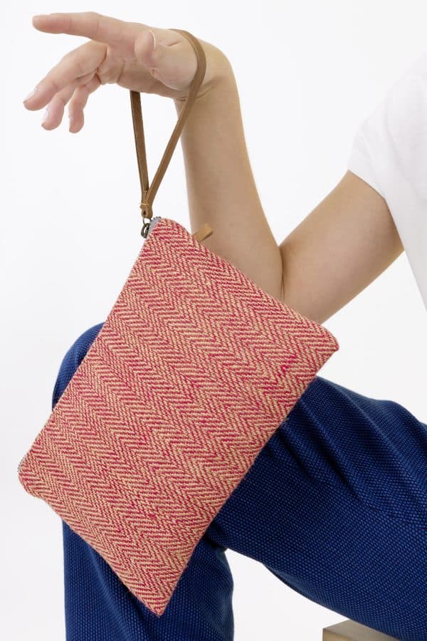Kwooksta herringbone jute clutch pouch in red hanging from hand by eco leather wrist strap